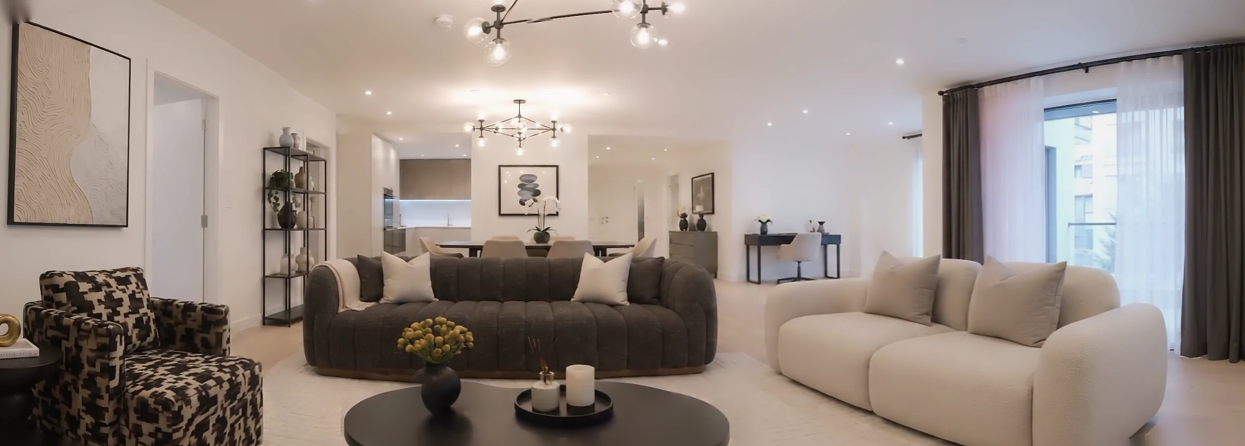 A bright open-plan living room with a patterned armchair, a deep charcoal sofa and a pale bouclé sofa by the window